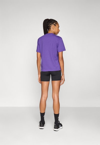 Lila rövid ujjú pamut póló, fekete rövidnadrággal párosítva. A póló laza szabású, sima tapintású, és nincs rajta látható minta.