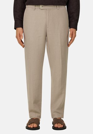 Beżowe spodnie o prostych nogawkach z zapięciem na guzik i zamek błyskawiczny, w połączeniu z brązowymi sandałami z odkrytymi palcami oraz ciemną bluzką z długim rękawem.