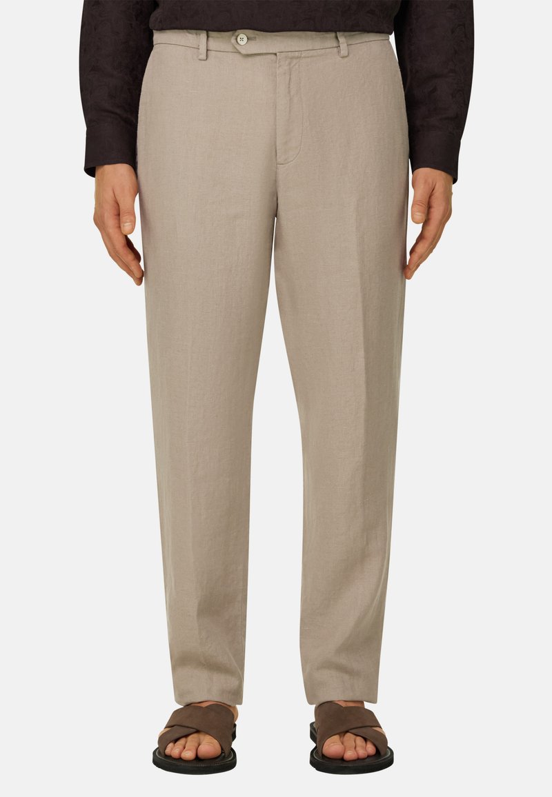 Pantalon beige à jambes droites avec fermeture par bouton et fermeture éclair, associé à des sandales ouvertes marron et un haut à manches longues foncé.