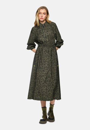 Grünes Leopardenmusterkleid mit Kragen, elastischem Bund und seitlichen Taschen. Kombiniert mit dunkelgrünen Stiefeletten.