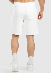 Weiße Baumwollshorts mit strukturierter Oberfläche, elastischem Bund und Gesäßtasche. Das Tragen von weißen Socken und Schuhen rundet den Look ab.
