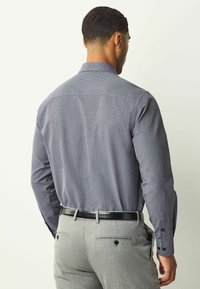 Cămașă pentru bărbați din țesătură albastră închisă cu un mic model geometric alb. Are mâneci lungi și guler, asortată cu pantaloni gri tailoring.