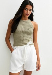 Haut halter en tricot olive avec un motif texturé, associé à un short en lin blanc avec un détail de taille nouée et des poches latérales.