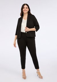 Sacou negru, tăiat pe corp, cu mâneci până la jumătate, asortat cu pantaloni negri strâmți și o bluză albă. Accentuat cu detalii din nasturi argintii.