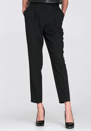 Czarne, dopasowane spodnie z plisami, posiadające boczne kieszenie, gładką fakturę oraz lekko zwężane nogawki, zestawione z czarnymi wysokimi obcasami.