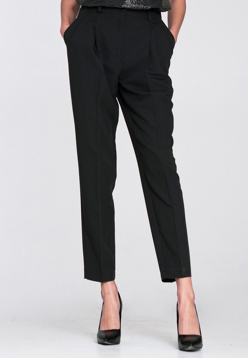 Czarne, dopasowane spodnie z plisami, posiadające boczne kieszenie, gładką fakturę oraz lekko zwężane nogawki, zestawione z czarnymi wysokimi obcasami.