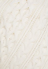 Tessuto lavorato a maglia bianco caratterizzato da un motivo a treccia testurizzato, con costine diagonali che attraversano la superficie, evidenziando la sua morbida e spessa consistenza.