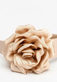 Beżowa satynowa opaska na głowę z wieloma warstwami płatków kwiatowych. Opaska jest gładka i szeroka, co dopełnia kwiatowy akcent.