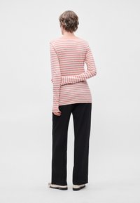 T-shirt de manga longa, riscas rosa e brancas, em tecido suave, com um design ajustado e gola redonda. Combinado com calças pretas de perna reta.