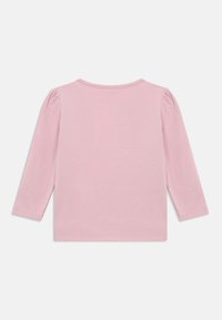 Ροζ μπλούζα για μωρά με μακριά μανίκια και ελαφρώς φουσκωτά μανίκια, απλός σχεδιασμός και στρογγυλή λαιμόκοψη, εμφανίζεται από την πίσω πλευρά σε λευκό φόντο.