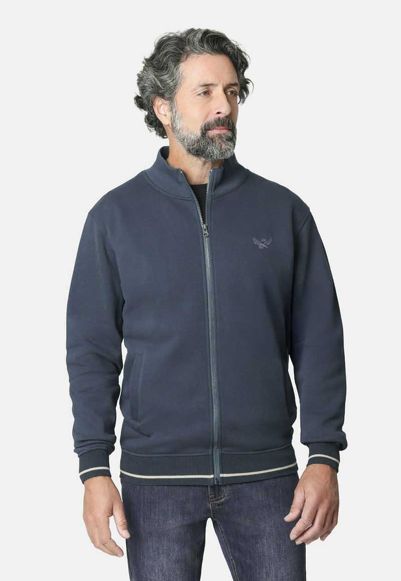 Chaqueta de cremallera en un azul marino oscuro, hecha de una tela suave, con un cuello alto, bolsillos laterales y puños acanalados con rayas en contraste.