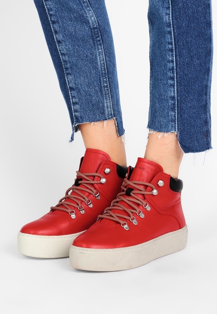 Czerwone skórzane wysokie sneakersy z okrągłymi sznurówkami i srebrnymi oczkami, z grubą białą podeszwą i czarnymi akcentami na kołnierzu.