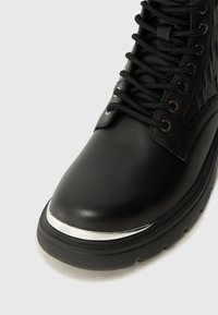 Black leather ankle boot with a glossy silver toe cap, textured side accents, and black laces. Features a sturdy black rubber sole.