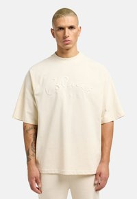 Kremfarget oversized t-skjorte laget av myk bomull. Har hevet broderi med "Colucci" tekst og rugby-stil raglanermer.