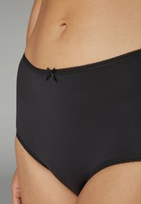 Czarne majtki z wysokim stanem, wykonane z gładkiego materiału, z koronkową lamówką wokół talii i małą kokardką na środku z przodu.