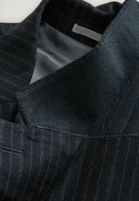 Kolor marynarki w ciemnym granacie z kołnierzem, wykonany z teksturowanej tkaniny filcowej, z dzianinowym wzorem w prążki na zewnętrznej stronie i gładką szarością podszewki.