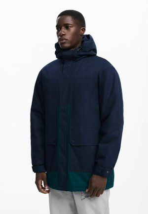 Navy hooded jacket with a mat finish, featuring green accents, dual front pockets, and a zipper closure. Smooth fabric with a structured design.