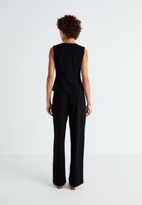 Un haut sans manches noir associé à un pantalon large noir. Le tissu semble lisse, avec une coupe ajustée qui met en valeur la silhouette.