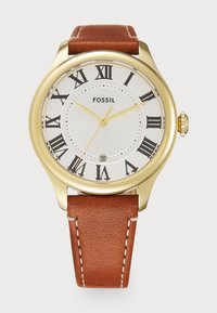 Montre dorée avec un cadran blanc et des chiffres romains noirs, un affichage de date, et un bracelet en cuir marron avec des coutures contrastantes.