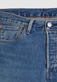 Blå denimjeans med metallknapp, bältesöglor, rundad framficka och synliga orange sömnadsdetaljer.