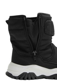 Schwarze isolierte Knöchelstiefel mit einem seitlichen Reißverschluss, gepolstertem Stoff-Obermaterial, dickem weißen Zwischensohleneinsatz und strukturierter schwarzer Gummisohle für Trittfestigkeit.