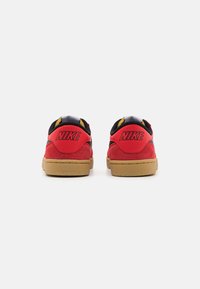Sneakers in suede rosso con accenti neri, suola in gomma e dettagli gialli sulla parte superiore. Presentano il logo "NIKE" sul tallone. Design low-top.
