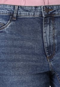 Denim jeans in dark blue with a subtle wash effect, featuring a classic five-pocket design and contrasting orange stitching at seams.