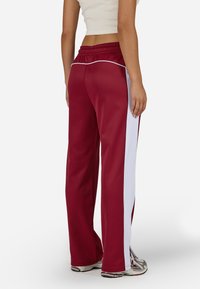 Czerwone spodnie sportowe z białymi paskami po bokach, charakteryzujące się luźnym krojem i elastyczną talią. Wykonane z gładkiego, elastycznego materiału.