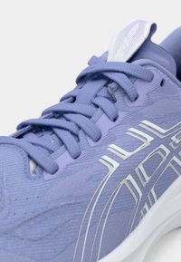 Hellblaues Sport Schuhwerk mit strukturiertem Obermaterial, flachen Schnürsenkeln und weißen Akzenten, gepolstertem Kragen und Logo auf der Zunge.