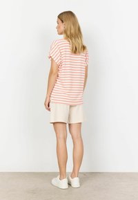 Stribet rosa og hvide kortærmede top med en løs pasform, parret med beige shorts og hvide sneakers. Glat stof, afslappet design.