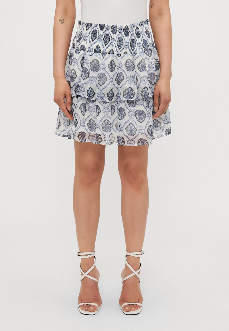 Valkoinen, kukkakuosisella hameella, jossa on rypsitty vyötärö ja kerrokselliset röyhelöt, yhdistettyinä valkoisiin remmillisiin korkokenkiin.