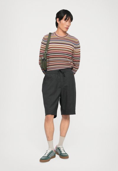 Pull à rayures à manches longues multicolore, short noir avec cordon de serrage, baskets vertes avec accents roses et chaussettes beiges.