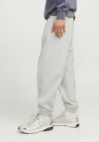 Light grey sweatpants with an elastic waistband and cuffs, made from soft material. Paired with textured, light metallic sneakers.