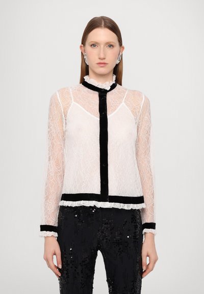 Blouse en dentelle blanche transparente avec col et accents en velours noir, dotée de manches longues, d'une fermeture à boutons et d'un ourlet et de poignets à volants.