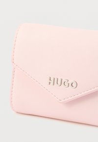 Ružová peňaženka z umelej kože so zapínaním na klapku, zdobená strieborným logom "HUGO" a detailmi stehovania. Hladká textúra s uhladeným dizajnom.