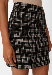 Schwarze Rock aus einem strukturierten Stoff mit einem Karo-Muster in Weiß und Hellrosa. Der Saum ist gerade und endet über dem Knie.