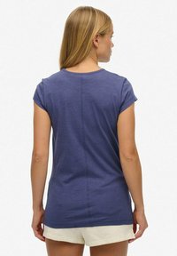 Top de manga corta en azul marino con cuello redondo, que presenta una sencilla costura en la parte posterior y un corte relajado, combinado con pantalones cortos claros.