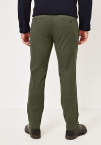 Olivgrüne Baumwollhosen mit geradem Schnitt, Gesäßtaschen und subtiler Textur, getragen mit schwarzen Schuhen und einem dunklen Pullover.