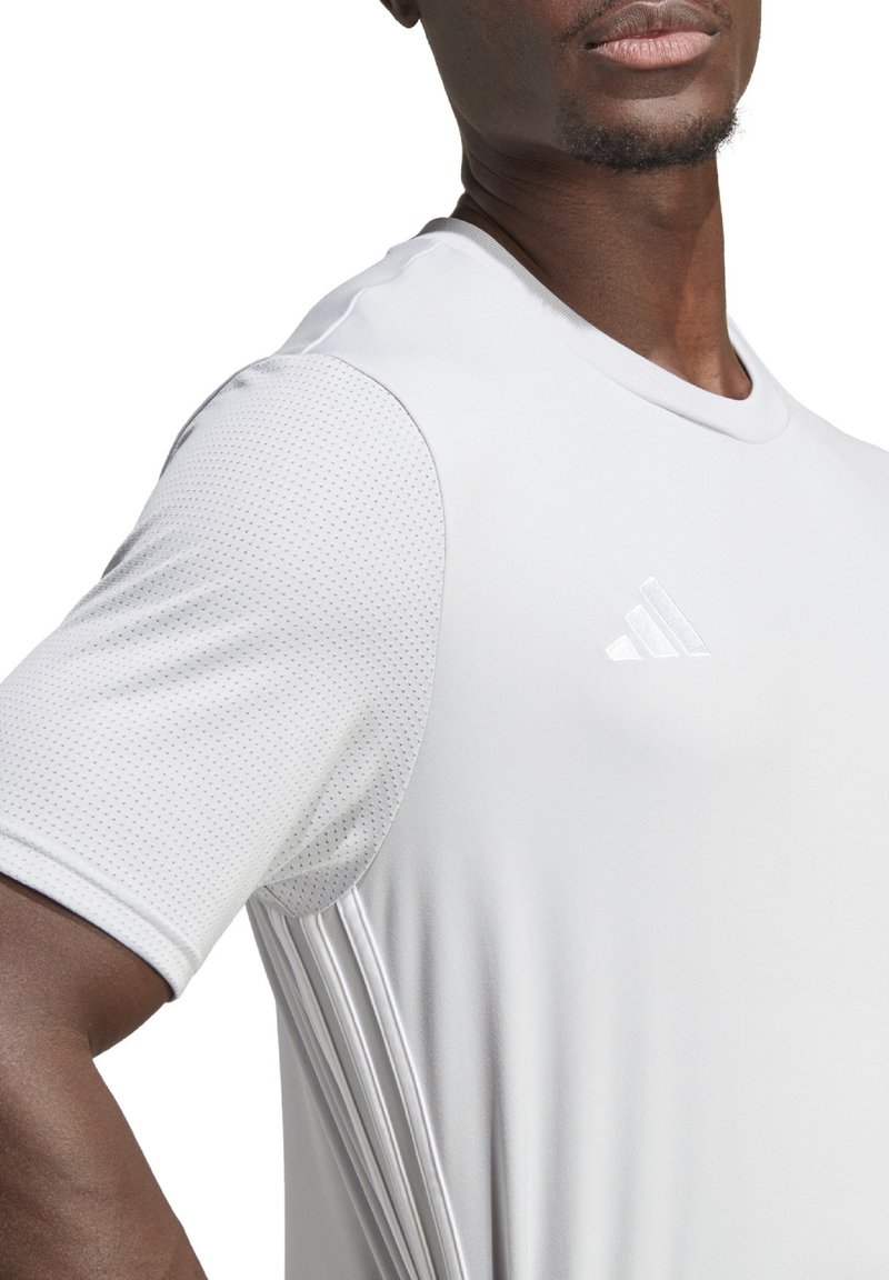 Lichtgrijs sportshirt met korte mouwen, ronde halslijn, textuuraccenten op de schouders en een subtiele drie-strepen detail aan de zijkant.
