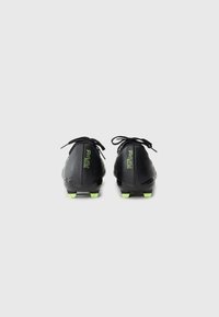 Botas de fútbol negras con tacos verde neón y la marca "Future", vistas desde la parte de atrás, atadas y colocadas sobre un fondo blanco liso.
