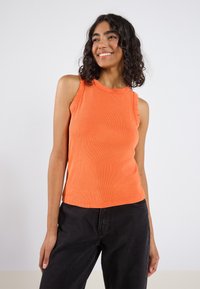 Orange ribbet tanktop med rund halsudskæring og uden ærmer, parret med sorte højtaljede bukser. Glat tekstur og tætsiddende stil.