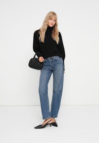 Juodas juostuotas megztinis, mėlynos tiesios kojos džinsai ir juodi smailiakojai slingback kulniukai. Maža struktūruota rankinė su rankenos detalėmis.
