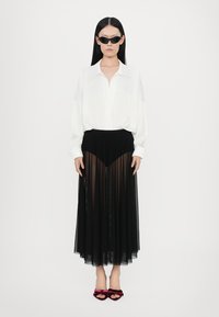 White, long-sleeve blouse, black sheer pleated skirt, and burgundy velvet shoes with floral accents. Sunglasses complete the outfit.
