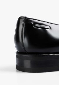 Zapato de vestir de cuero negro con un acabado suave, forma redondeada y un tacón bajo y sólido negro. Presenta costuras sutiles y un lazo en el costado.