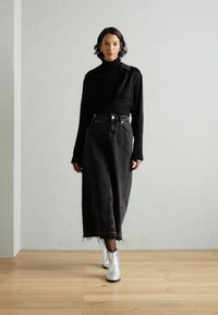 Un suéter de cuello alto negro combinado con una larga falda de mezclilla negra y botas de tobillo plateadas. Textura suave con detalles en el dobladillo deshilachado de la falda.