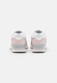 Helle rosa Wildleder-Sneaker mit weißen Akzenten, ausgestattet mit einer grauen Zwischensohle und einer erhöhten, strukturierten Ferse. „New Balance“-Logo auf der Ferse.