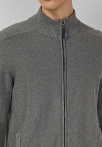 Grijze gebreide cardigan met ritssluiting en een geribbelde kraag, met een gladde textuur en subtiele naden op de schouders en zijkanten.