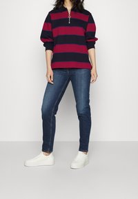 Långärmad polotröja med marinblå och vinröda ränder, med dragkedja i halsen. Kombinerad med blå smala jeans och vita sneakers.