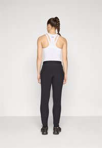 Vit sporttopp med racerback-design och logotyp, tillsammans med svarta avsmalnande sweatshirtbyxor och svarta träningsskor. Enkel, funktionell stil.