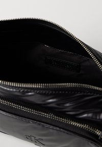 Μαύρη δερμάτινη θήκη με λεία υφή και κλείσιμο με φερμουάρ. Διαθέτει λογότυπο αποτυπωμένο μπροστά και μαύρη επένδυση εσωτερικά.